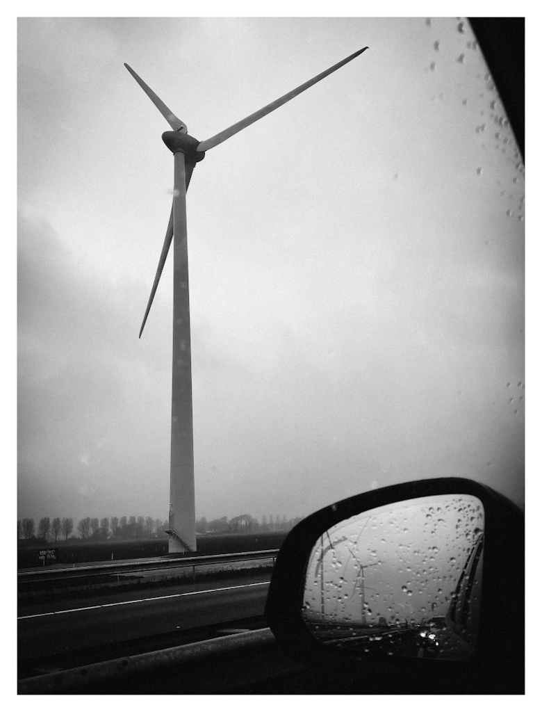A windmill on the left, the rear view mirror of a car on the right. Viewed from inside a car. 
