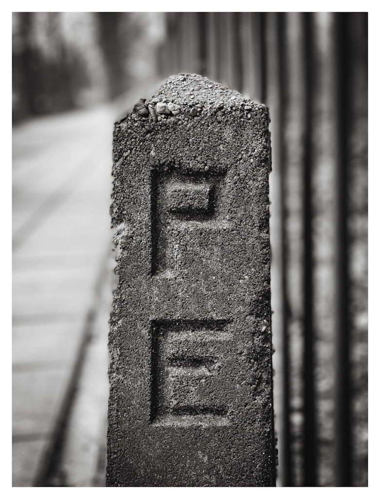 An upright standing concrete stone with the letters P and E on it. 