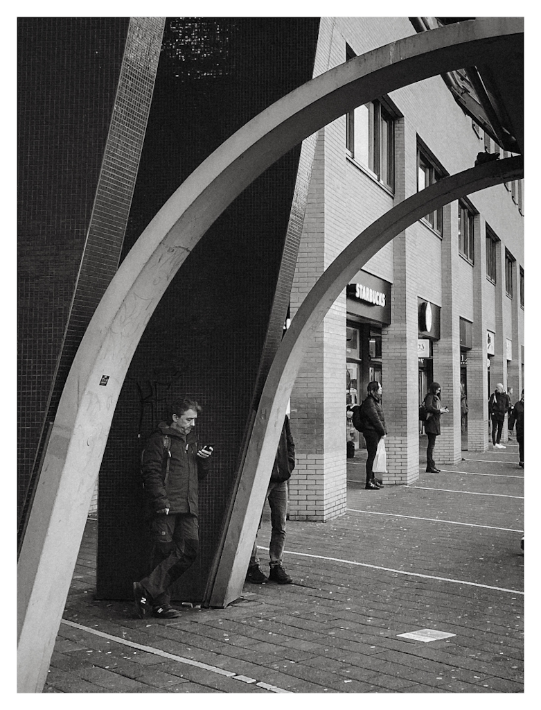 People waiting patiently under arches, in black and white. 
