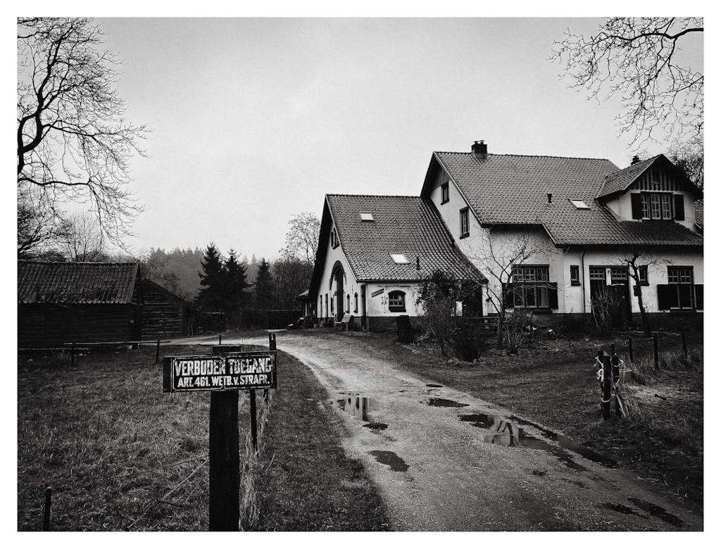 No trespassing sign in front of a classic farm house in the rain. In black and white. 