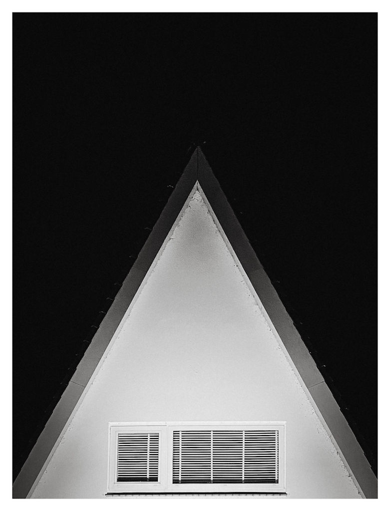 The triangle shaped upper floor of a white house, against a dark night sky. 