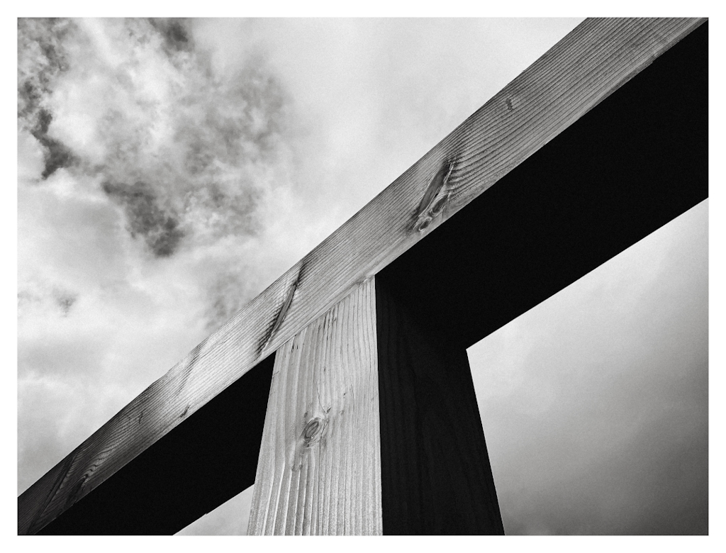 Looking up at detail of a wooden construction, with only triangles visible against a cloudy sky. In black and white. 