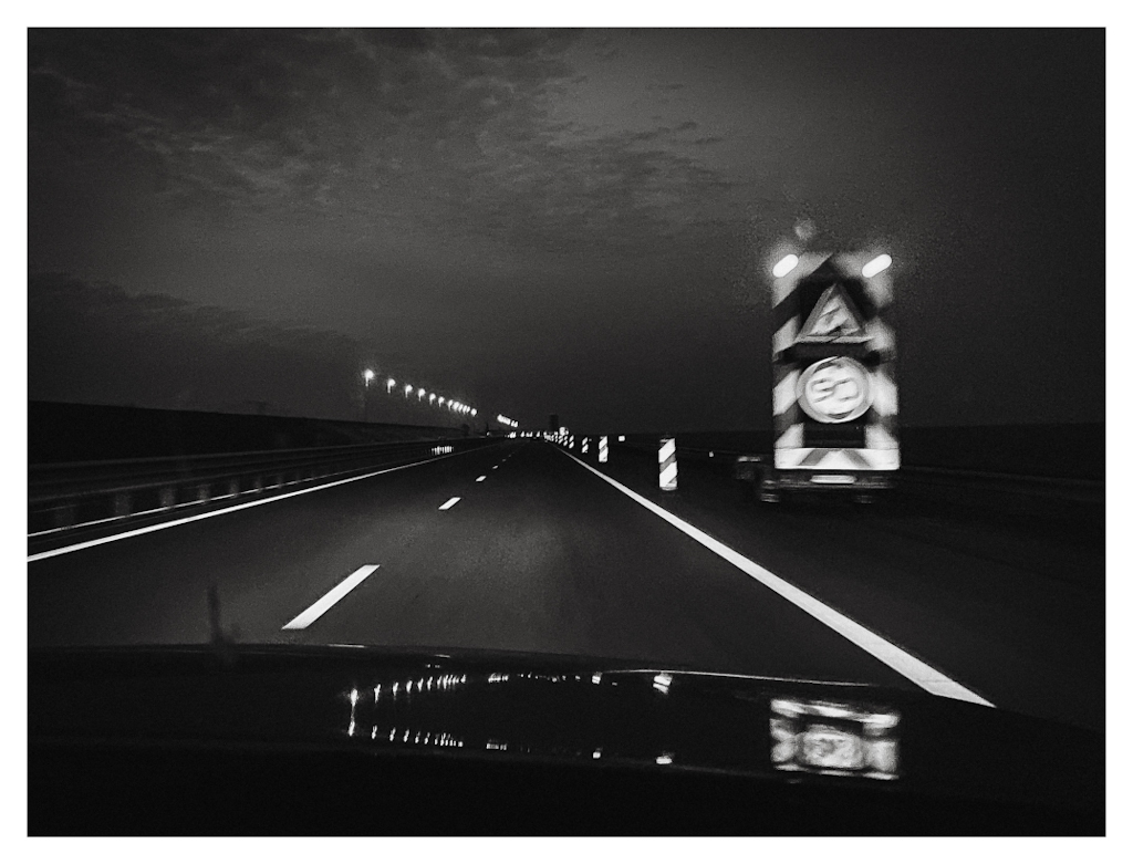 Shot from a driving car, the lines of a road reflecting the headlights in the dark of the night. 