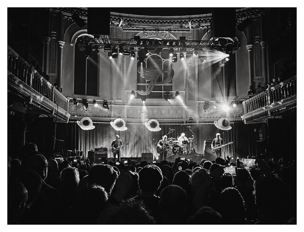 The Pixies on stage in Paradiso Amsterdam, with the crowd in front of it, in black and white. 