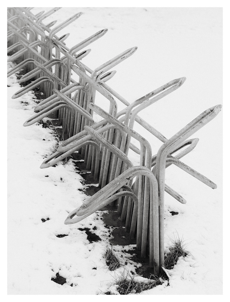 Diagonal row of bicycle racks in the snow, in black and white. 