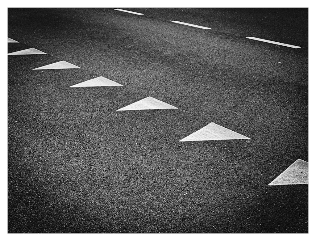 White triangles on a black asphalt road, lined diagonally. 
