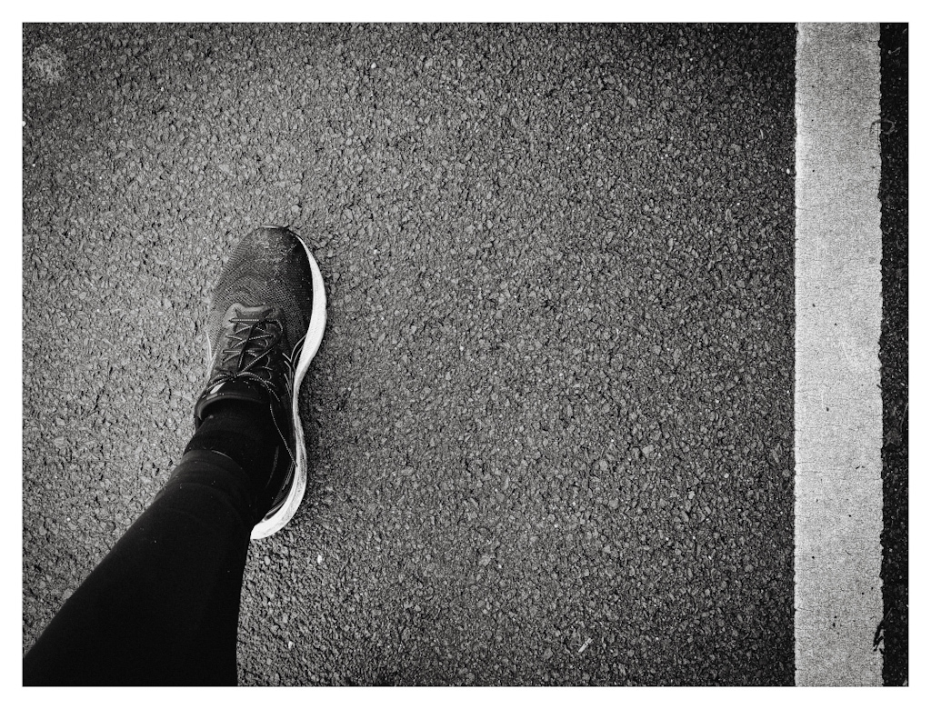 View down on the road, showing a running leg in black and white on the left and a road line on the right. 